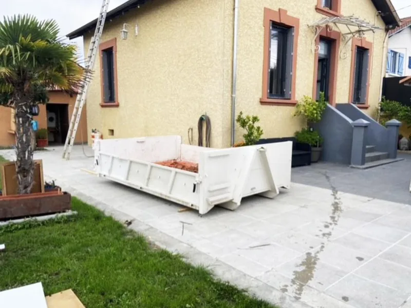 Benne de 3 m³ posée sur une terrasse devant une maison en rénovation